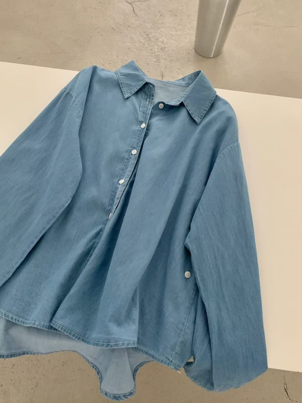 Light blue denim shirt - flat lay on white surface
