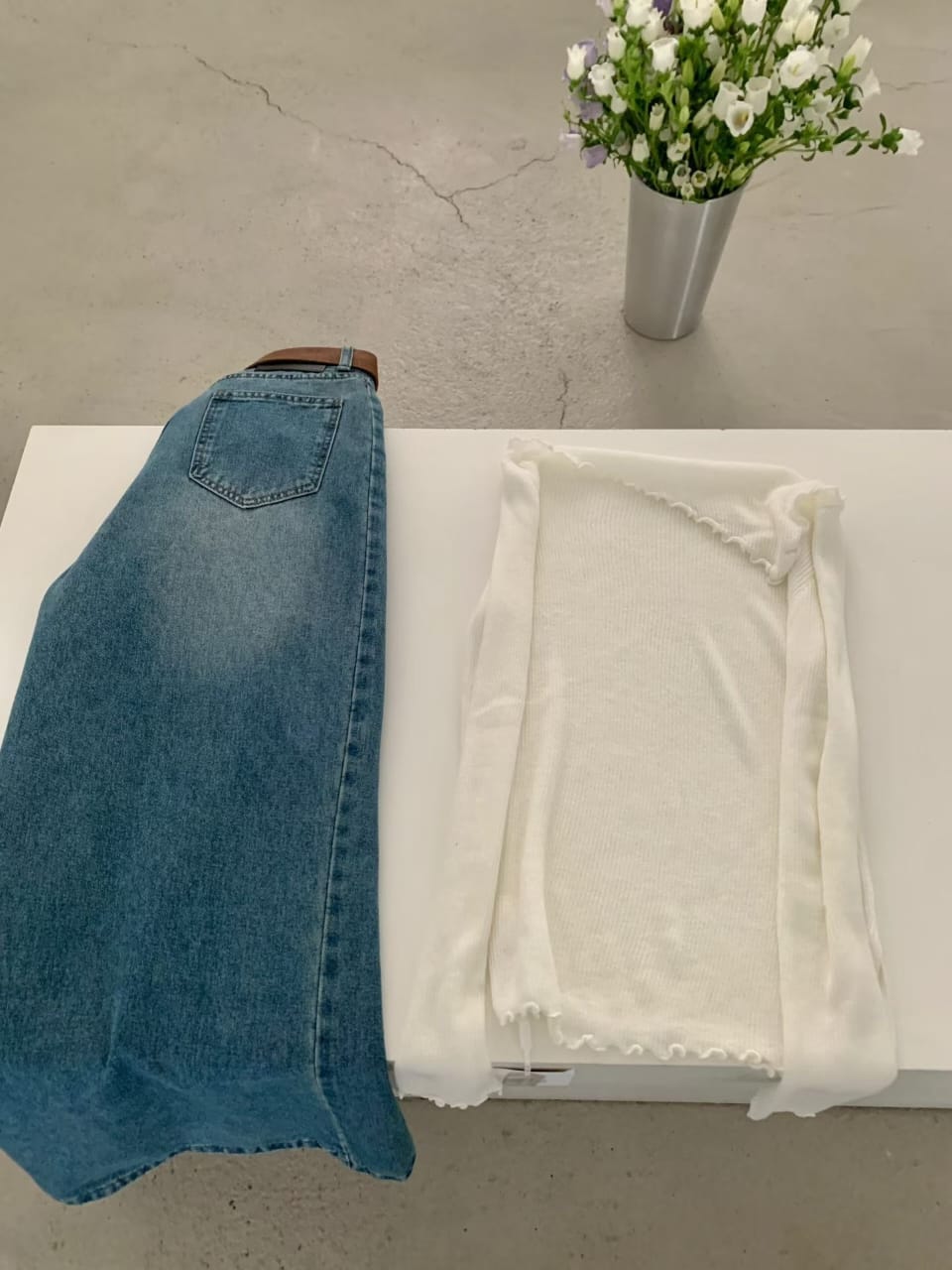 White off-shoulder ribbed knit top and wide-leg jeans - flat lay with brown belt